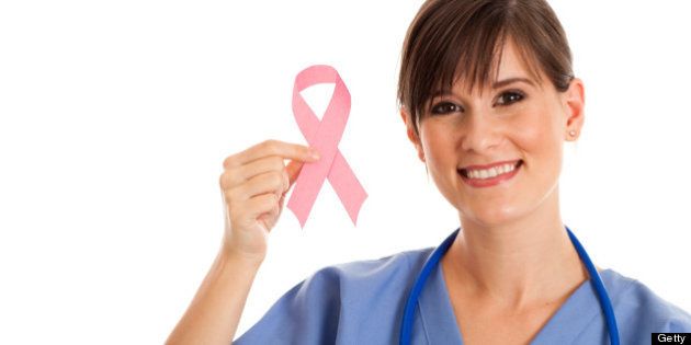 Color photo of a happy, female nurse holding up a Breast Cancer Awareness Ribbon on white background.