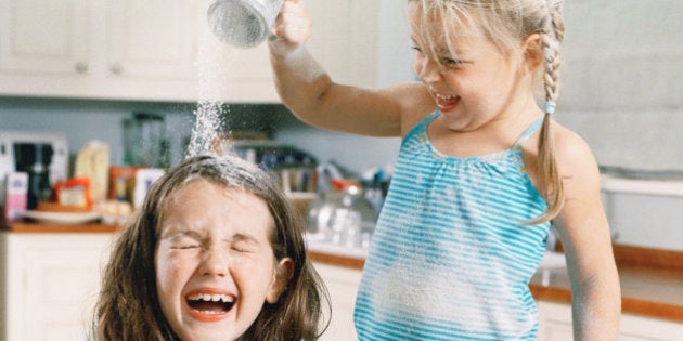 Two girls (5-8) preparing dough, one pouring flour over other's head