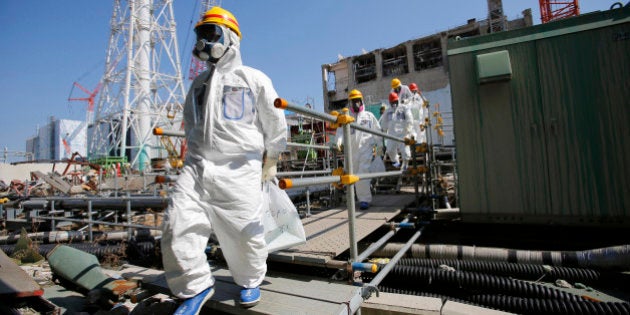 Members of the media and Tokyo Electric Power Co. (Tepco) employees, wearing protective suits and masks, walk towards the common spent fuel facility during a visit to the company's Fukushima Dai-Ichi nuclear power plant in Okuma, Fukushima Prefecture, Japan, on Wednesday, March 6, 2013. Tepco's Fukushima Dai-Ichi plant had three reactor core meltdowns after it was hit by an earthquake and tsunami on March 11, 2011. Photographer: Issei Kato/Pool via Bloomberg