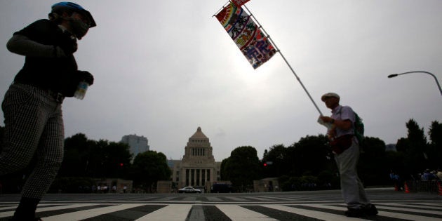 A protester holds a banner in front of the National Diet building during a rally in Tokyo, Sunday, June 14, 2015. About 25,000 protesters gathered outside parliament, opposing a set of controversial bills intended to expand Japanâs defense role at home and internationally. (AP Photo/Shizuo Kambayashi)