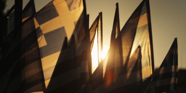 ATHENS, GREECE - JULY 05: The sun sets through Grrek flags over the Greek parliament as the polls have now closed in the Greek austerity referendum and people are begining to gather in the squares of Athens waiting for the official result on July 5, 2015 in Athens, Greece. The people of Greece are going to the polls to decide if the country should accept the terms and conditions of a bailout with its creditors. Greek Prime Minister Alexis Tsipras is urging people to vote 'a proud no' to European creditors' proposals, and 'live with dignity in Europe'. 'Yes' campaigners believe that a no vote would mean financial ruin for Greece and the loss of the Euro currency. (Photo by Christopher Furlong/Getty Images)