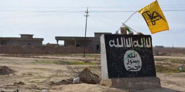 A flag of the Shiite Hezbollah militant group flutters over a mural depicting the emblem of the Islamic State (IS) group in Al-Alam village, northeast of the multi-ethnic Iraqi city of Tikrit, on March 9, 2015, during a military operation by Iraqi government forces and tribal fighters to regain control of the Tikrit region from jihadists. After being forced out of the province of Diyala earlier this year, the IS jihadists are now fighting off a huge assault on the city of Tikrit as government and allied forces continue to work their way north towards the main IS stronghold of Mosul. AFP PHOTO / YOUNIS AL-BAYATI (Photo credit should read YOUNIS AL-BAYATI/AFP/Getty Images)