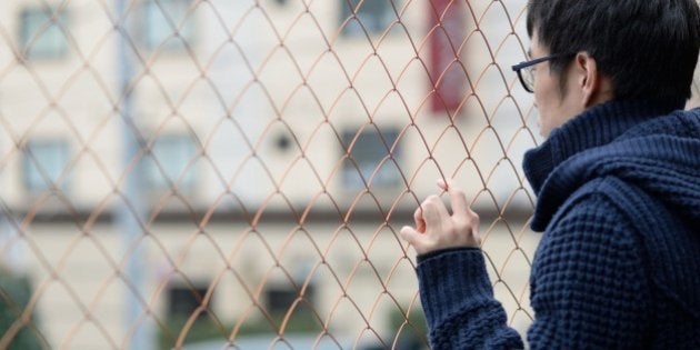 A young man standing behind a fence.