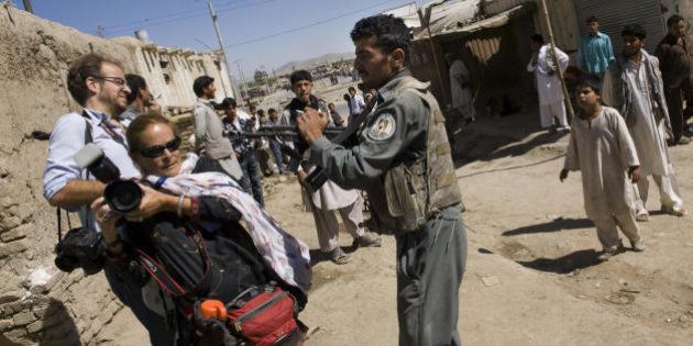 An Afghan policeman aims his weapon at photojournalists Paula Bronstein (2L) and Kevin Frayer (L) as he prevents them from approaching the area where three gunmen stormed a bank in Kabul on August 19, 2009. The Afghan government came under severe criticism for attempting to ban media coverage of escalating Taliban violence in case it deters people from voting in Thursday's elections. AFP PHOTO/PEDRO UGARTE (Photo credit should read PEDRO UGARTE/AFP/Getty Images)