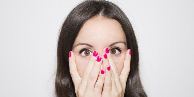 Close-up portrait. Surprise, fear and horror.Woman covering her face with two hands hand and looking between her fingers.