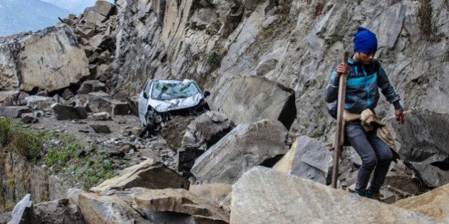 In this Monday, April 27, 2015 photo, a Nepalese man walks over fallen rocks and past a crushed car on the way to Dhunche, Nepal, a village in Langtang National Park, two days after a 7.8-magnatude earthquake hit the region. The photographer, Joe Sieder, said the man was part of a group of Nepalese workers and trekkers who left Syabrubesi earlier that day and hiked about 30 km (19 miles) for 13 hours, mostly over boulder-strewn roads with some small landslides along the way to make their way to a passable road. (Joe Sieder via AP) MANDATORY CREDIT