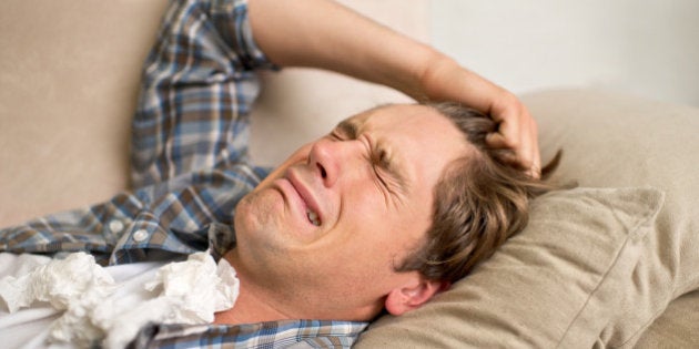 A young man crying while lying on the sofa with tissues