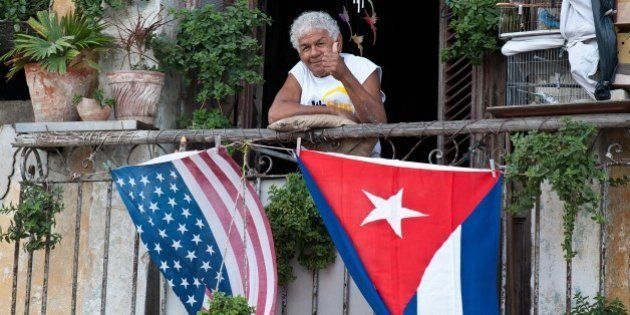 A Cuban gives the thumbs up from his balcony decorated with the US and Cuban flags in Havana, on January 16, 2015. The United States will ease travel and trade restrictions with Cuba on Friday, marking the first concrete steps towards restoring normal ties with the Cold War-era foe since announcing a historic rapprochement. AFP PHOTO/YAMIL Lage (Photo credit should read YAMIL LAGE/AFP/Getty Images)