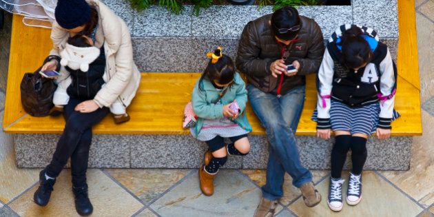 Kawasaki, Kanagawa Prefecture, Japan - March 8, 2015: People sitting on bench in a shopping mall are texting on their mobile phones.