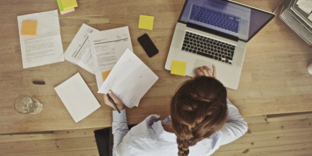 High angle view of an young brunette working at her office desk with documents and laptop. Businesswoman working on paperwork.