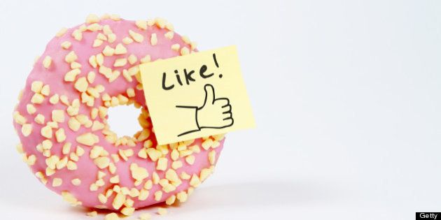 A pink donut with a 'like' symbol sticky note attached to it on a white background.