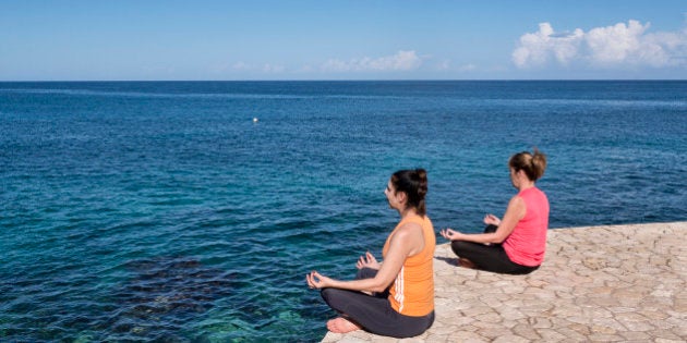 NEGRIL, WEST END, WESTMORELAND PARISH, JAMAICA - 2014/01/10: Two women practice yoga from a waterfront ledge. (Photo by John Greim/LightRocket via Getty Images)