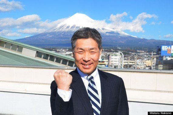 富士山を背にポーズをとる静岡県富士市産業支援センターの小出宗昭さん＝12月18日、静岡県富士市
