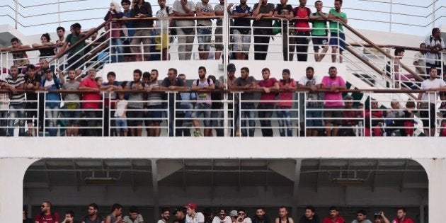 Migrants stand the hull of the Greek government-chartered Eleftherios Venizelos ferry upon their arrival at the port of Piraeus on August 21, 2015. A Greek government-chartered ferry transported another 2,000 mainly Syrian migrants to the Greek mainland from the island of Lesbos, as islands struggling with an influx of migrants warned that the crisis is endangering public health. AFP PHOTO /LOUISA GOULIAMAKI (Photo credit should read LOUISA GOULIAMAKI/AFP/Getty Images)