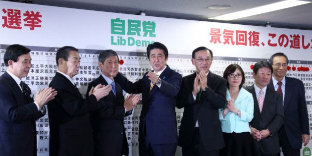 Shinzo Abe, Japan's prime minister and president of the Liberal Democratic Party (LDP), center, places a red paper rose on an LDP candidate's name to indicate a lower house election victory with other party executives including Sadakazu Tanigaki, secretary general, fourth from right, Masahiko Komura, vice president, third from left, and Toshimitsu Motegi, chairman of the Election Strategy Committee, second from right, at the party's headquarters in Tokyo, Japan, on Sunday, Dec. 14, 2014. Abe's ruling coalition won Japan's general election, according to an NHK exit poll, which also indicates the bloc may maintain its two-thirds majority in the lower house. Photographer: Tomohiro Ohsumi/Bloomberg via Getty Images