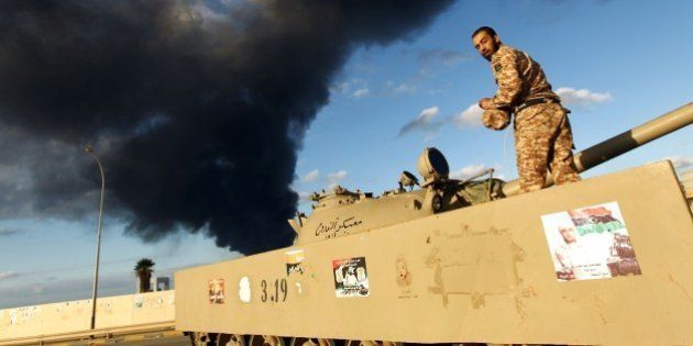 A member of the Libyan army stands on a tank as heavy black smoke rises from the city's port in the background after a fire broke out at a car tyre disposal plant during clashes against Islamist gunmen in the eastern Libyan city of Benghazi on December 23, 2014. Forces loyal to former general Khalifa Haftar and to internationally recognised Prime Minister Abdullah al-Thani have been battling for weeks against Islamists who have taken control of much of Libya's second city, and the capital Tripoli. AFP PHOTO / ABDULLAH DOMA (Photo credit should read ABDULLAH DOMA/AFP/Getty Images)