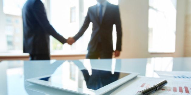 Business objects at workplace with handshaking partners on background