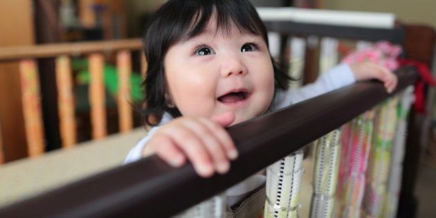 cute baby girl doing peek a boo in a customized crib