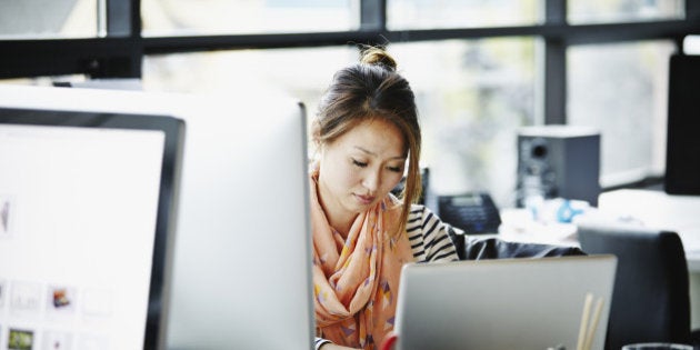 Businesswoman sitting at desk in high tech startup office working on laptop