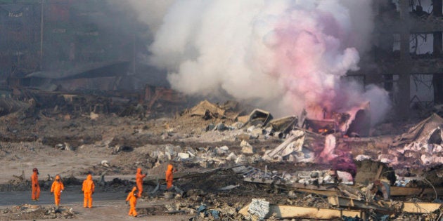 Fire fighters in protective gear watch partially pink smoke continue to billow after an explosion at a warehouse in northeastern China's Tianjin municipality, Thursday, Aug. 13, 2015. Huge, fiery blasts at a warehouse for hazardous chemicals killed many people and turned nearby buildings into skeletal shells in the Chinese port of Tianjin, raising questions Thursday about whether the materials had been properly stored. (AP Photo/Ng Han Guan)