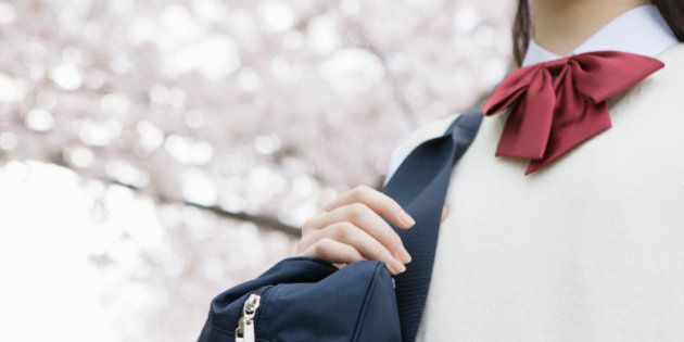 Teenage girl in school uniform smiling by cherry tree, mid section