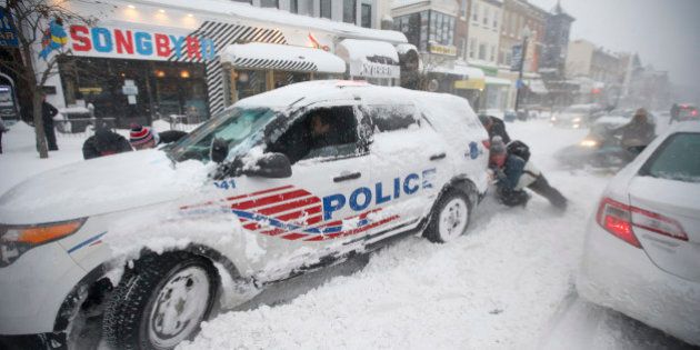 People pitch in to get a DC Metro police car moving again on 18th Street NW, Saturday, Jan. 23, 2016 in Washington. A blizzard with hurricane-force winds brought much of the East Coast to a standstill Saturday, dumping as much as 3 feet of snow, stranding tens of thousands of travelers and shutting down the nation's capital and its largest city. (AP Photo/Alex Brandon)