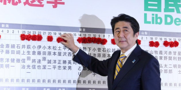 Shinzo Abe, Japan's prime minister and president of the Liberal Democratic Party (LDP), places a red paper rose on a LDP candidate's name to indicate a lower house election victory, at the party's headquarters in Tokyo, Japan, on Sunday, Dec. 14, 2014. Abe's ruling coalition won Japan's general election, according to an NHK exit poll, which also indicates the bloc may maintain its two-thirds majority in the lower house. Photographer: Tomohiro Ohsumi/Bloomberg via Getty Images