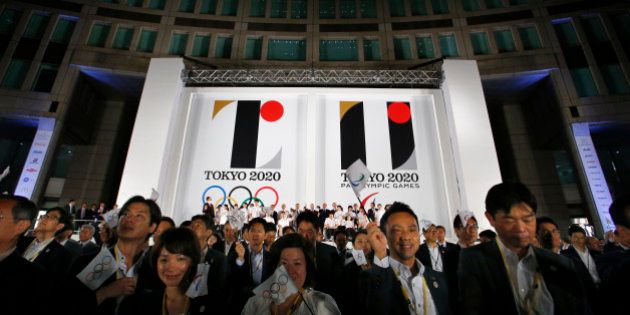 Visitors wave a flag for the Olympics and Paralympics in front of a official Emblems of the Tokyo 2020 Olympic and Paralympic Games at Tokyo Metropolitan Plaza in Tokyo, Friday, July 24, 2015. (AP Photo/Shizuo Kambayashi)