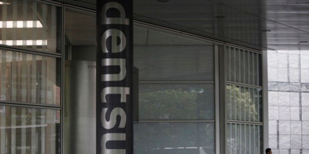 A man speaks on his mobile phone near a logo of Dentsu Co. at the entrance of the company headquarters in Tokyo July 12, 2012. Japanese ad giant Dentsu is buying marketing group Aegis for 3.2 billion pounds ($5 billion), the biggest deal in its history as it seeks to expand outside its home market with the British firm's European and digital business. REUTERS/Issei Kato (JAPAN - Tags: BUSINESS MEDIA LOGO)