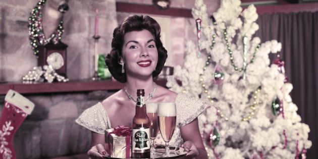 Portrait of an unidentified model as she stands in front of a Christmas tree next to a fireplace with a bottle of Pabst Blue Ribbon beer, two glasses, and a present on a serving tray, 1951. (Photo by Tom Kelley/Getty Images)