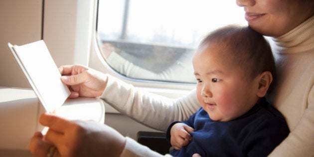 Asian mother is reading a book to her baby on train.