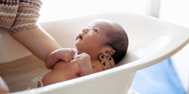 A woman bathing her baby in baby bathtub. A baby is looking up at her.