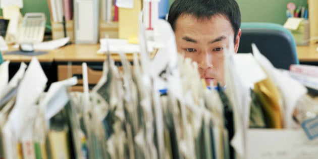 Businessman at desk, view over row of files (focus on man's face)