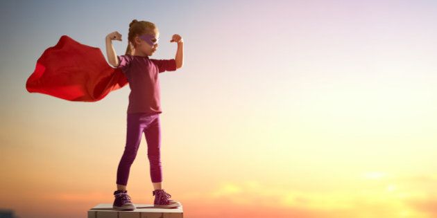 Little child girl plays superhero. Child on the background of sunset sky. Girl power concept