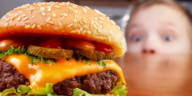 Hungry young boy is staring and smelling a hamburger on wooden table