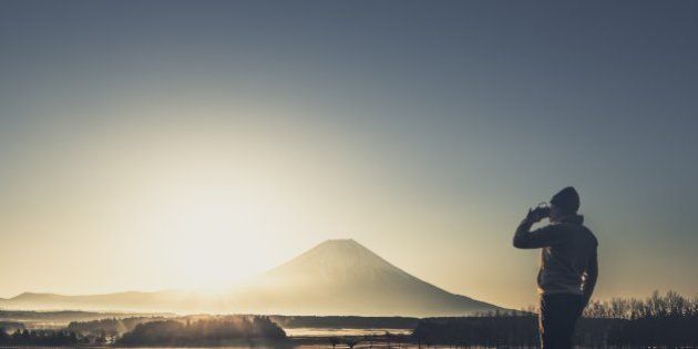 View of man drinking coffee in front of Mt. Fuji at sunrise.