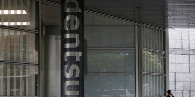 A man speaks on his mobile phone near a logo of Dentsu Co. at the entrance of the company headquarters in Tokyo July 12, 2012. REUTERS/Issei Kato/File photo