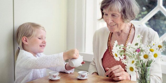 Girl pouring tea into a tea cup and her grandmother sitting beside her