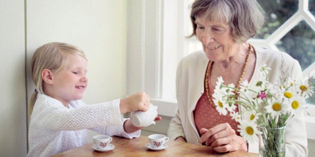 Girl pouring tea into a tea cup and her grandmother sitting beside her