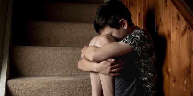 Sad, bullied or abused boy crying sitting on stairs