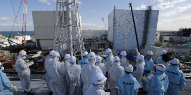 Members of the media, wearing protective suits and masks, receive briefing from Tokyo Electric Power Co. (TEPCO) employees (in blue) in front of the No. 1 and No.2 reactor buildings at TEPCO's Fukushima Daiichi nuclear power plant in Okuma town, Fukushima prefecture, Japan, on Feb. 10, 2016. March 11, 2016 is the 5th anniversary of the massive earthquake and tsunami that caused a meltdown at TEPCO's Fukushima Dai-Ichi facility. Photographer: Toru Hanai/Pool via Bloomberg