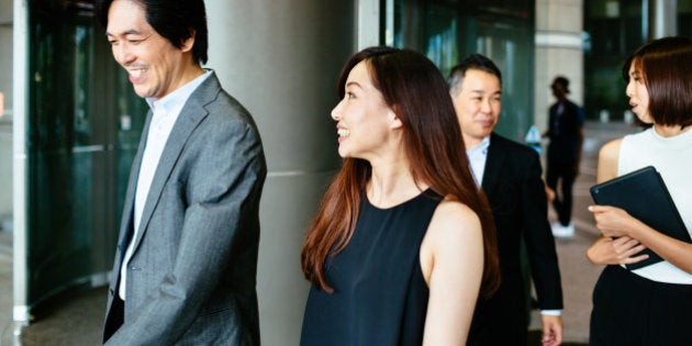 Group of japanese business people leaving an office building. They're talking and walking through a swing door