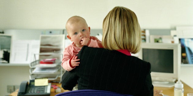 Woman working at desk holding baby girl (9-12 months), rear view