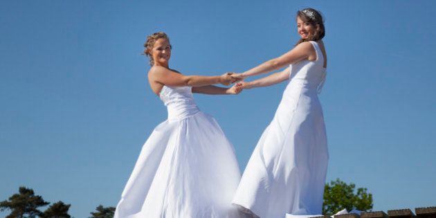 two brides on wooden bridge against blue sky background hold each other