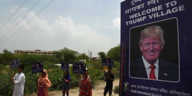 Indian children hold placards next to a billboard with the image of US President Donald Trump by the entrance gate of Marora village, which has been unofficially renamed 'Trump Village,' about 100km from New Delhi, on June 23, 2017.A rural Indian settlement with little electricity or running water renamed itself 'Trump Village' on June 23 in an unusual gesture to the American president ahead of Prime Minister Narendra Modi's trip to Washington. A huge billboard declaring 'Welcome to Trump Village' in Hindi and English, accompanied with a beaming portrait of the US president, was unveiled in Haryana state's Marora, as the village is officially known. The water and sanitation group Sulabh, which has been installing toilets in the impoverished settlement, suggested the name change to the local council. / AFP PHOTO / MONEY SHARMA (Photo credit should read MONEY SHARMA/AFP/Getty Images)