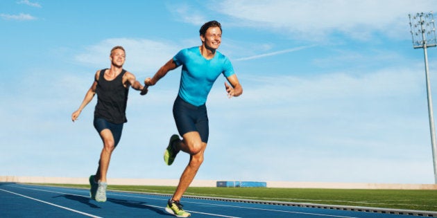 Shot of professional male athletes passing over the baton while running on the track. Athletes practicing relay race on racetrack.