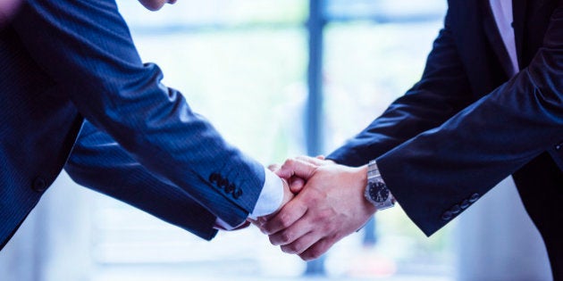 Japanese businessmen shaking hands and bowing toward each other in office building.