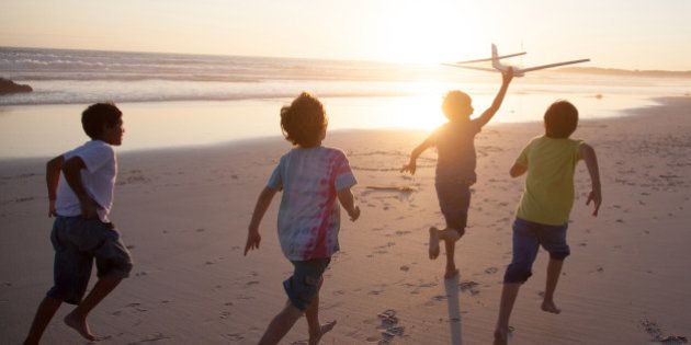 Boys, aged 9-10, running along a beach at sunset with a toy plane