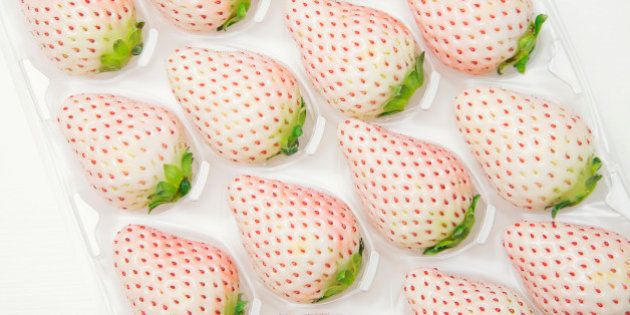 A box of fresh, ripe pink strawberries on white wooden table.