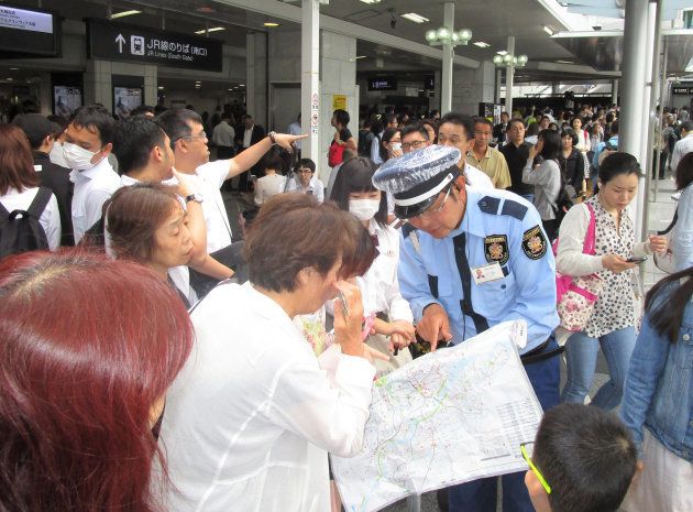地震の影響で電車が止まり、警備員にバスの行き先を確認する人たち＝１８日午前９時半すぎ、ＪＲ大阪駅前 撮影日：2018年06月18日